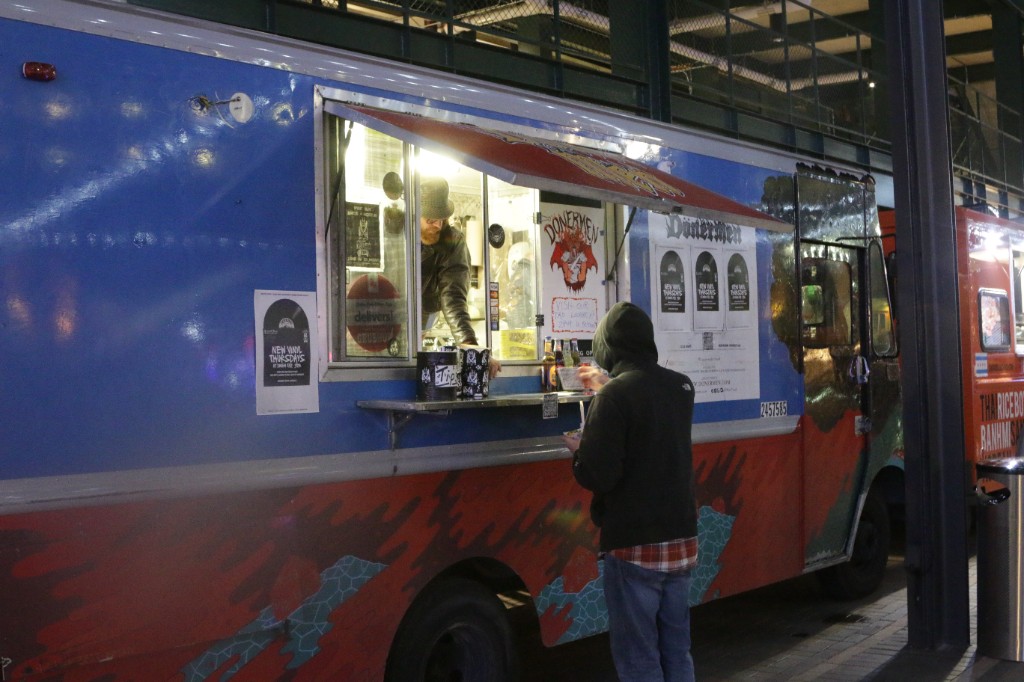 Close-up of a food truck menu and warm interior lighting with guests waiting outside