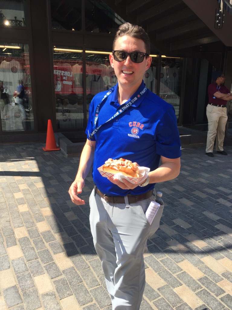Guest in a Cubs polo holding a lobster roll outside the team store at Wrigley Field