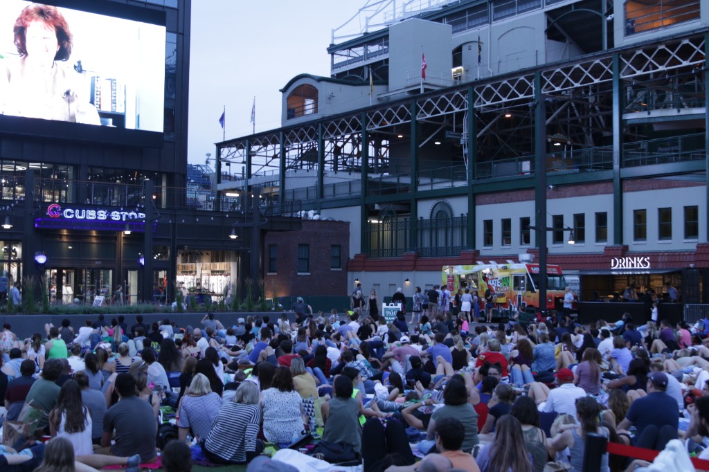 Audience in folding chairs watching a film on the plaza screen next to Wrigley Field