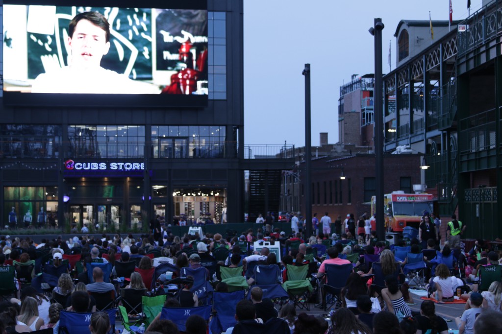 Evening movie night with a packed lawn audience and the Cubs Store sign glowing